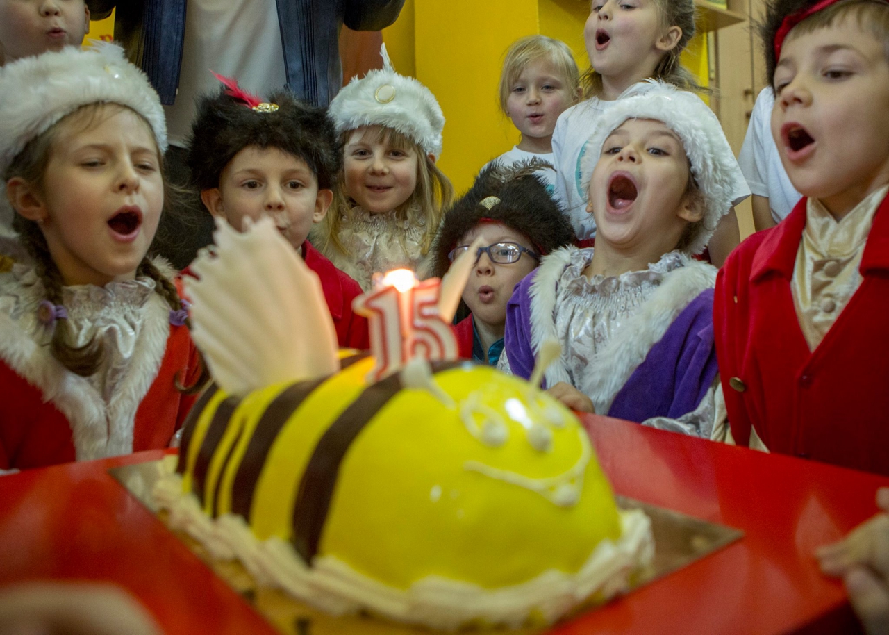 Przedszkolaki w strojach bożonarodzeniowych zdmuchują świeczkę na torcie.