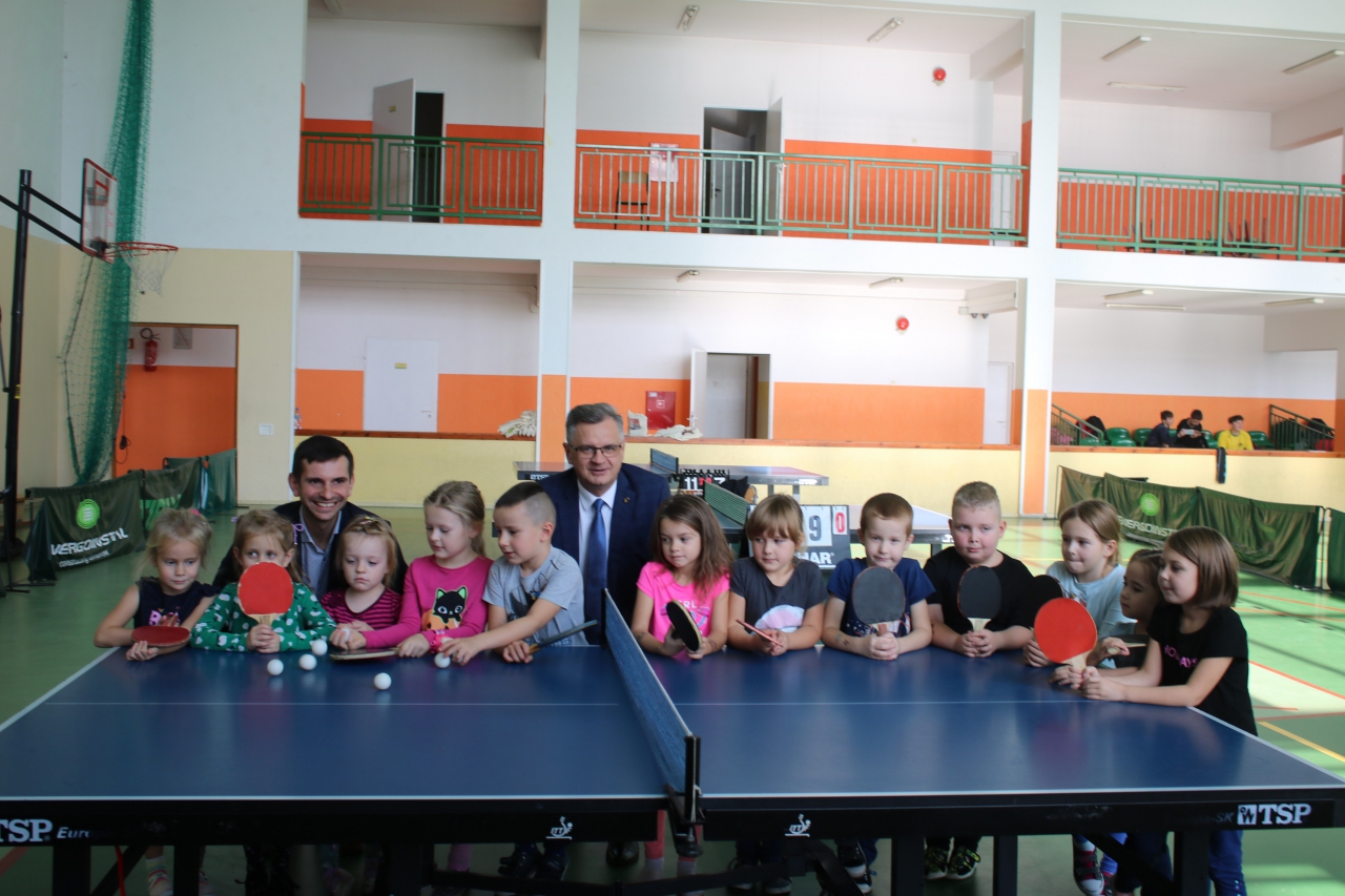 Władze powiatu wraz z dziećmi przy stole tenisowym w hali sportowej