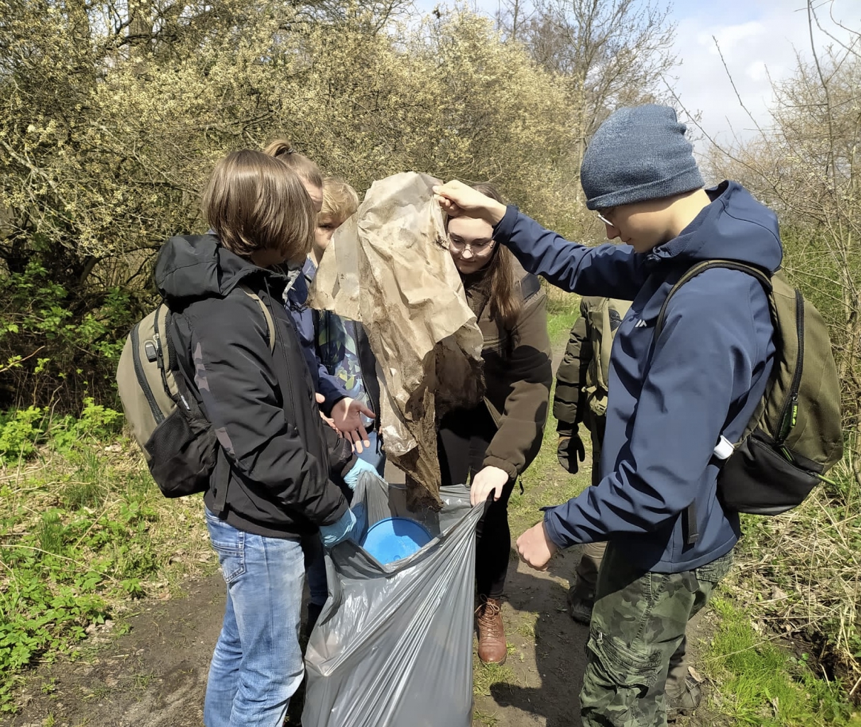 Młodzież ze szkoły w Bujnach wrzuca śmieci do worka zebrane podczas sprzątania lasu na Wierzejach
