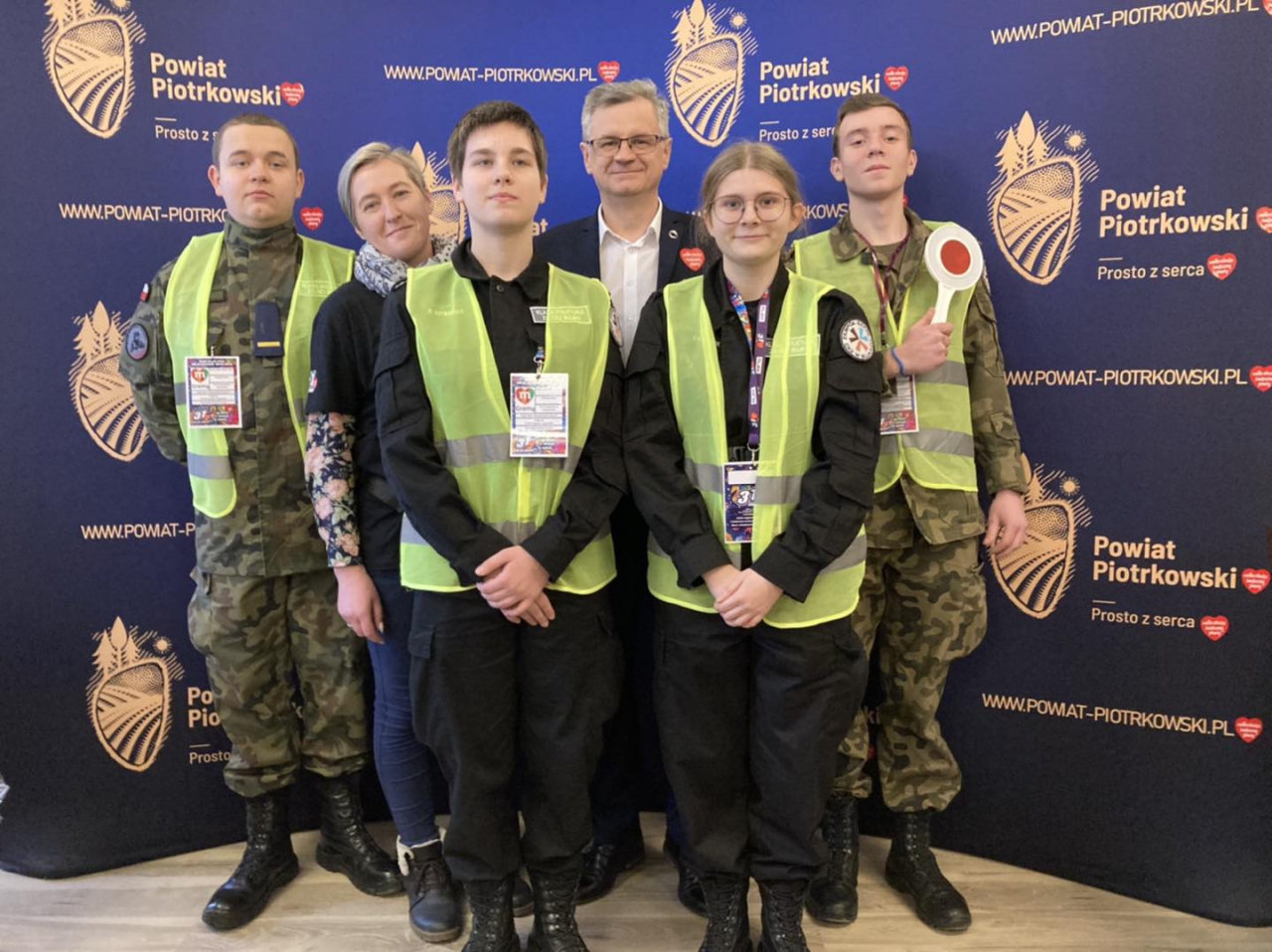 Wicestarosta Dariusz Magacz z uczniami z Bujen znajdują się w banku sztabowym. w tle ścianka z logo powiatu piotrkowskiego prosto z serca.