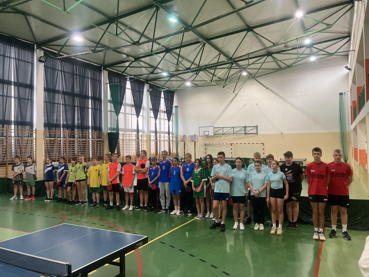 Uczestnicy wydarzenia stoją w hali sportowej