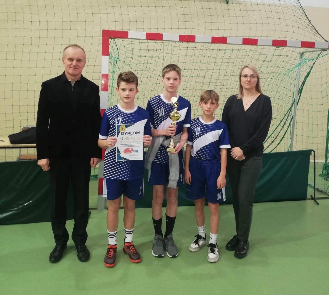 Jedna ze zwycięskich drużyn chłopców stoi w hali sportowej z pucharem