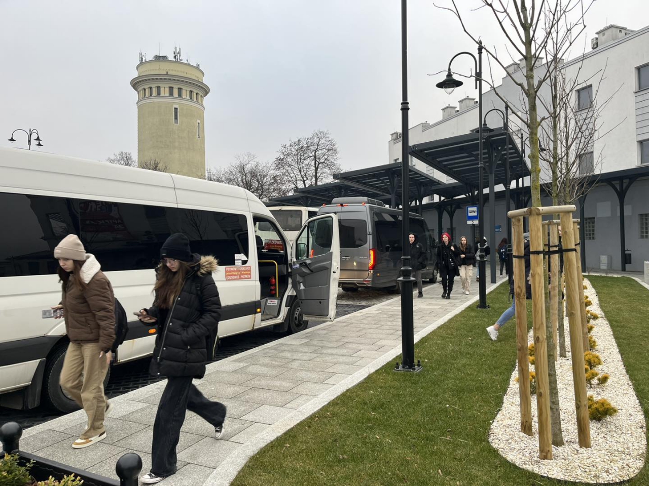 Pasażerowie na terenie Powiatowego Centrum Przesiadkowego Piotrków Trybunalski. W tle Wieża Ciśnień.