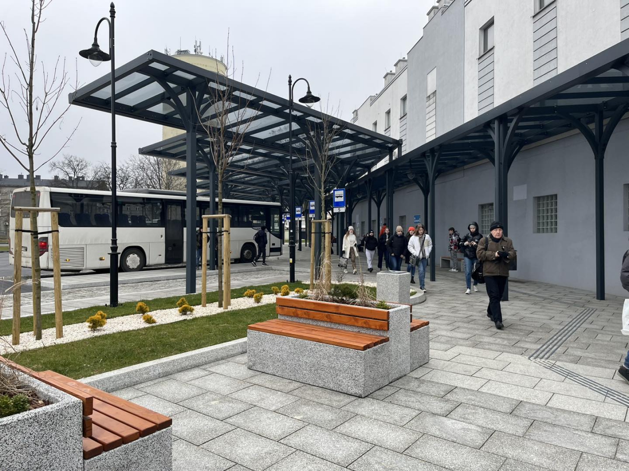 Pasażerowie na terenie Powiatowego Centrum Przesiadkowego Piotrków Trybunalski. W tle Wieża Ciśnień.