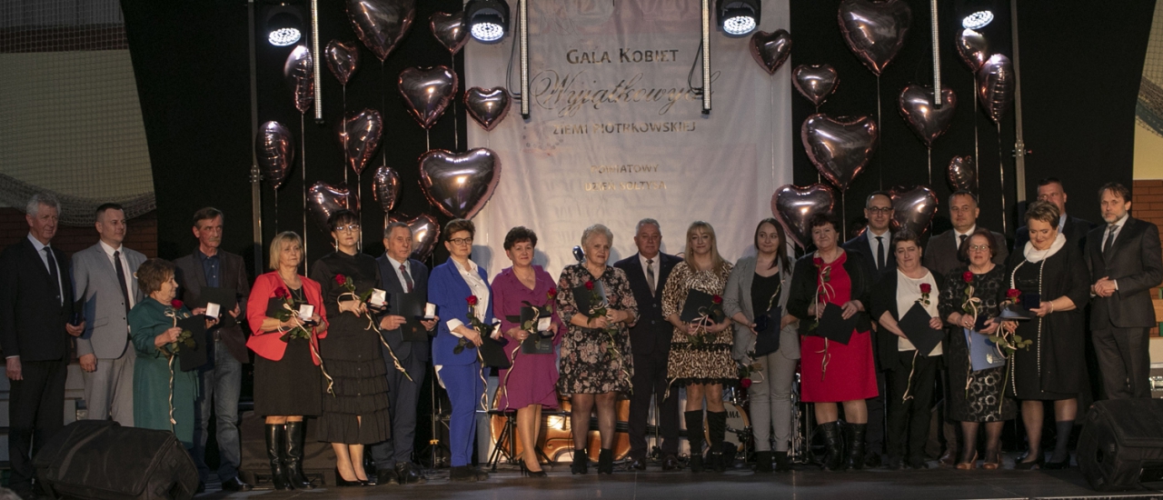 Nagrodzone osoby stoją na scenie w sali w Moszczenicy wraz ze Starostą Piotrem Wojtysiakiem oraz zaproszonymi gośćmi.W tle napis Gala Kobiet Wyjątkowych Ziemi Piotrkowskiej.