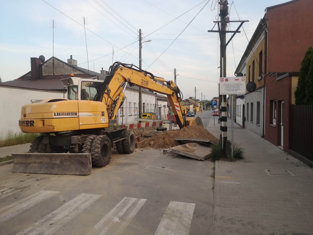 Koparka stoi na ulicy , przejazd ogranicza barierka