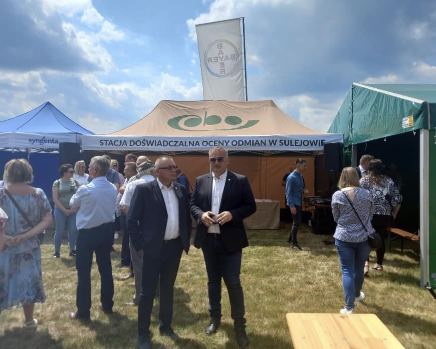 Dwóch mężczyzn stoi, w tle namioty i inni ludzie